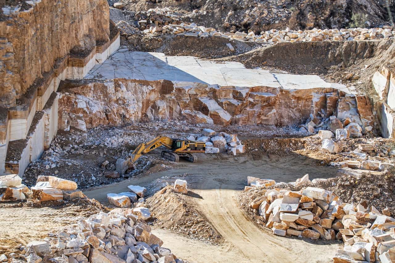 An excavator operating in a large stone quarry with rugged rocky terrain under daylight