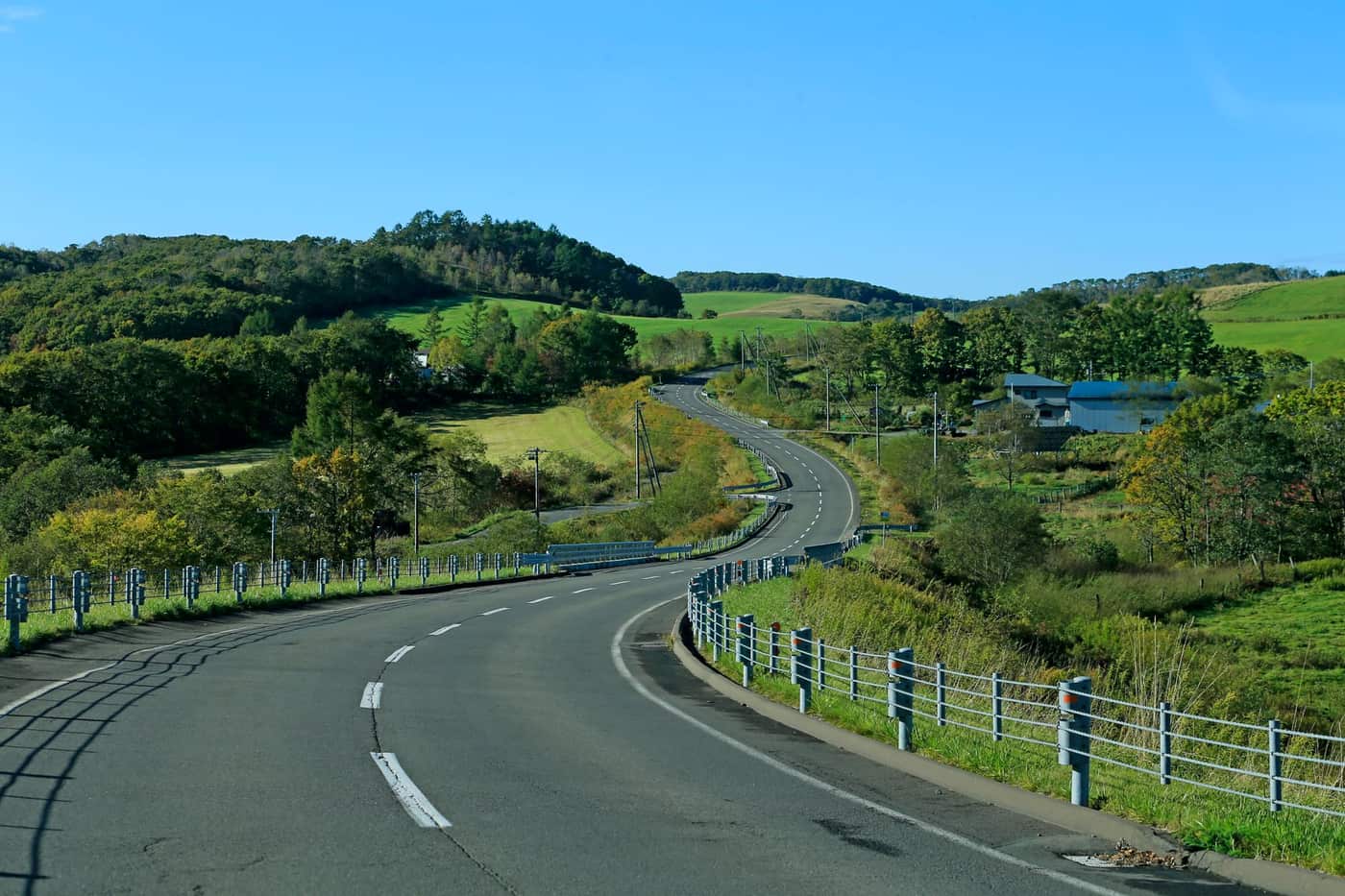 Empty rural road winding through green hills under a clear sky