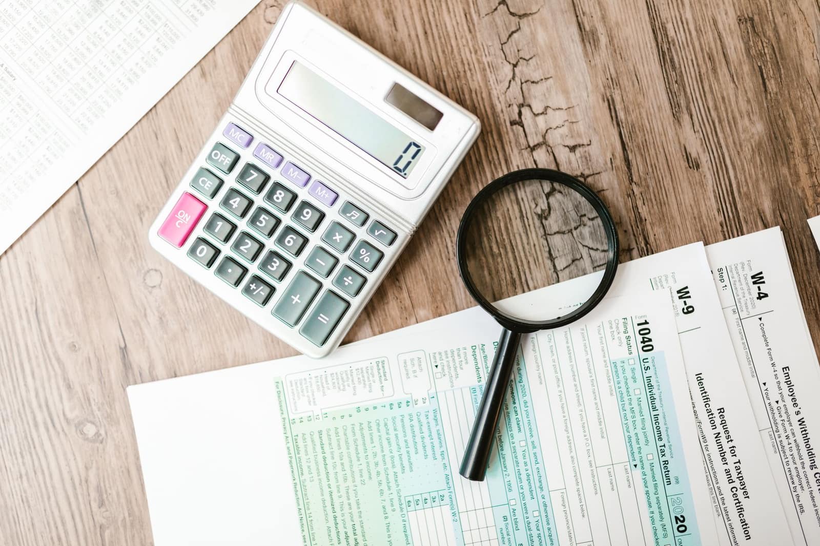 Tax forms laid out with a calculator and magnifying glass on a wooden surface