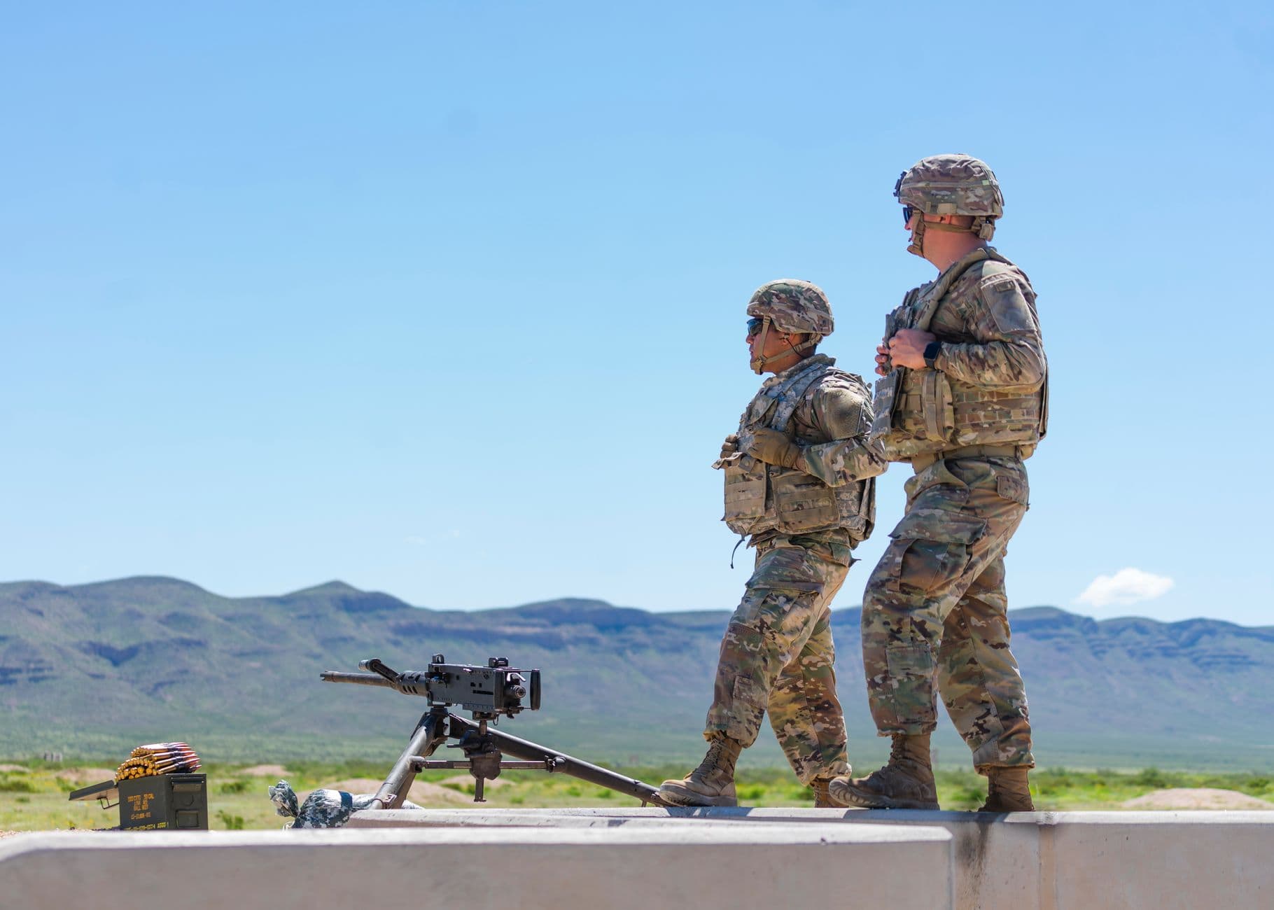 Two soldiers in uniform standing beside a rifle during outdoor training