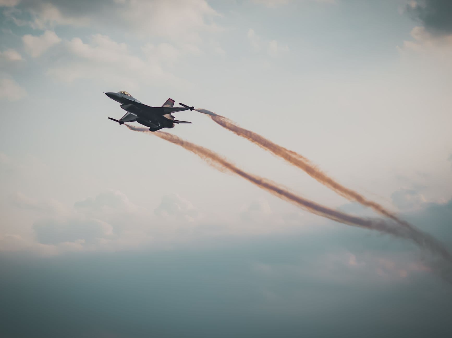 A military fighter jet flying through a cloudy sky