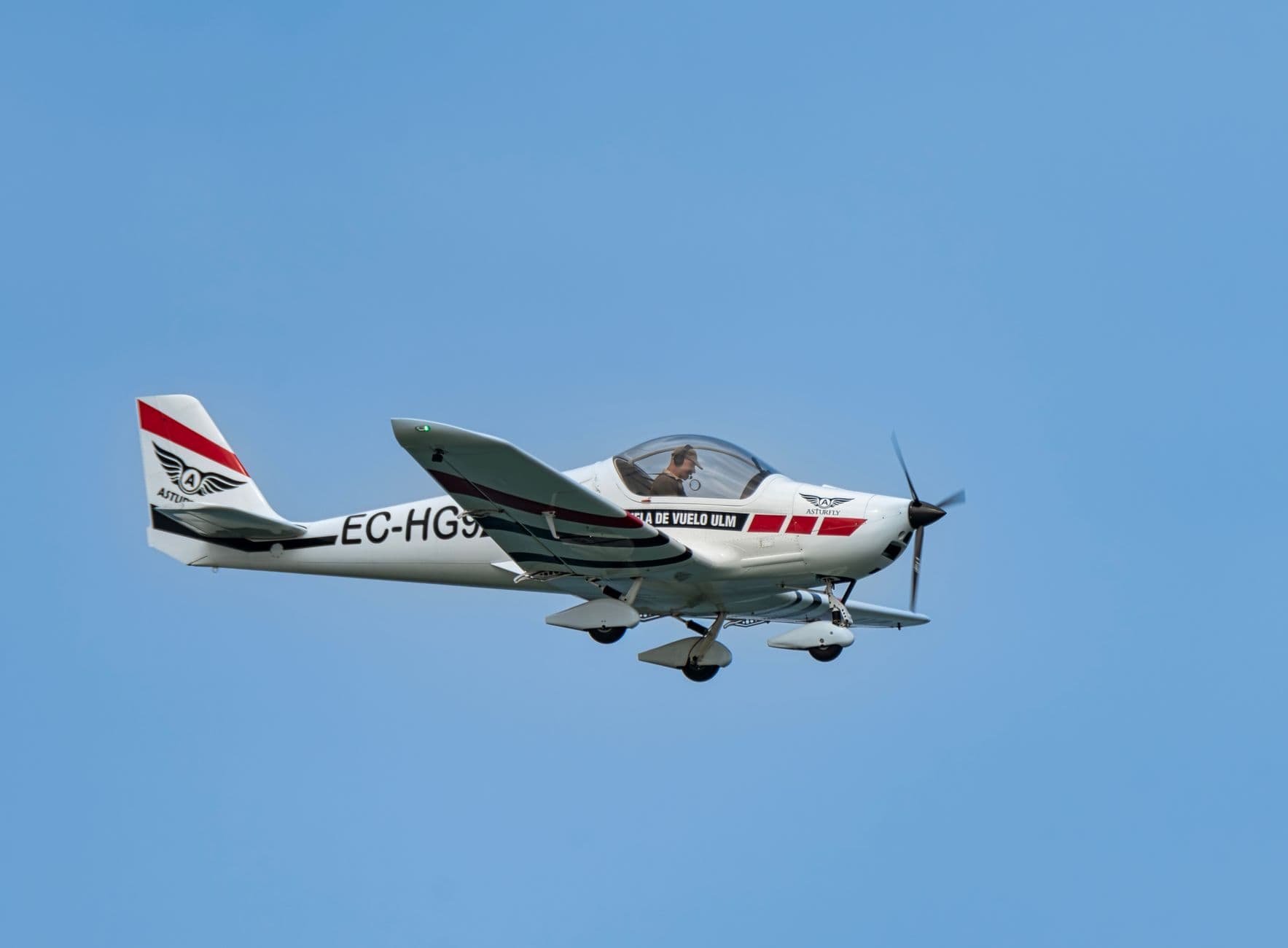 A small single-engine propeller aircraft in flight against a clear blue sky