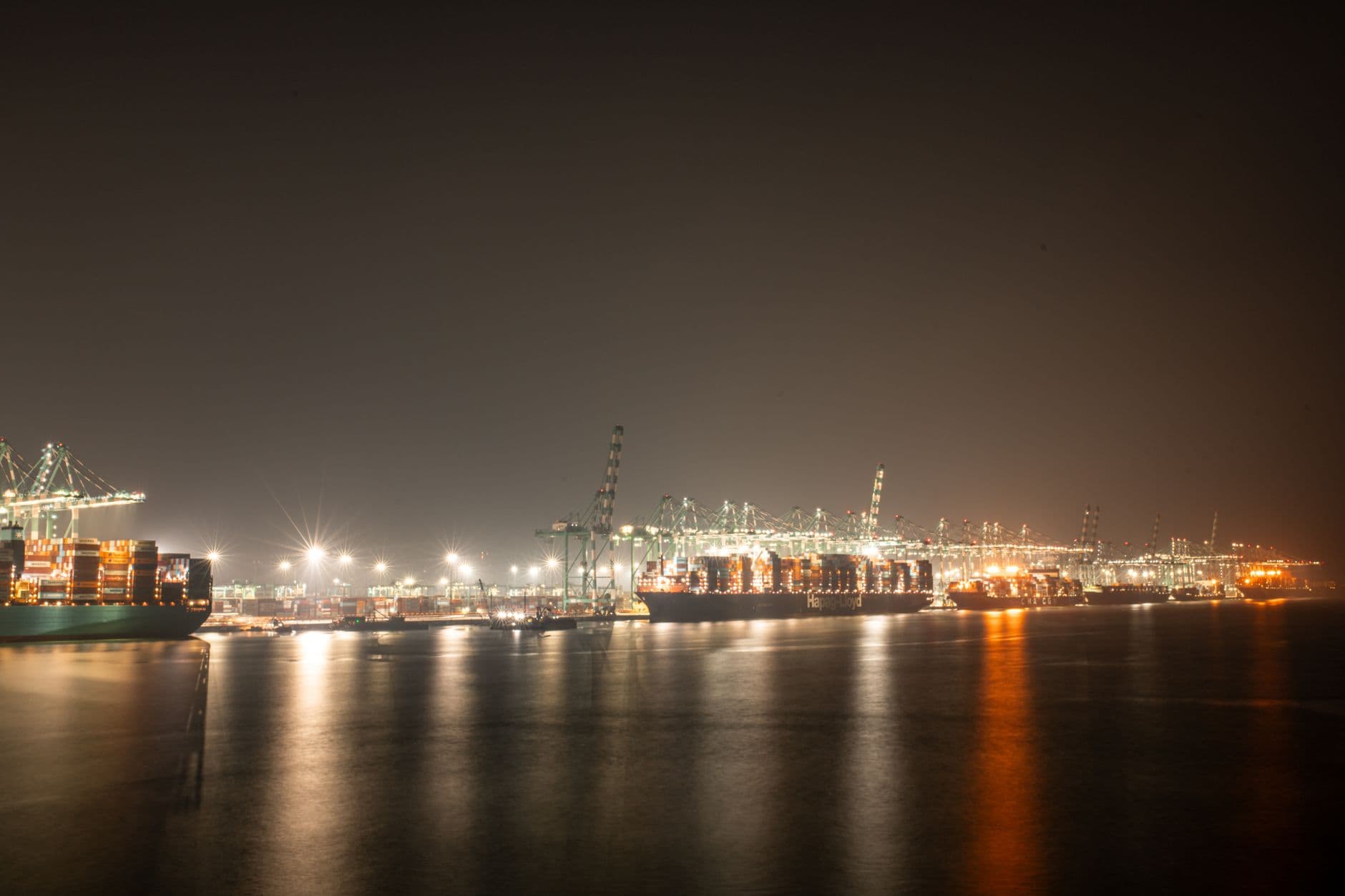 Cargo ships and stacked shipping containers at a busy commercial port at night