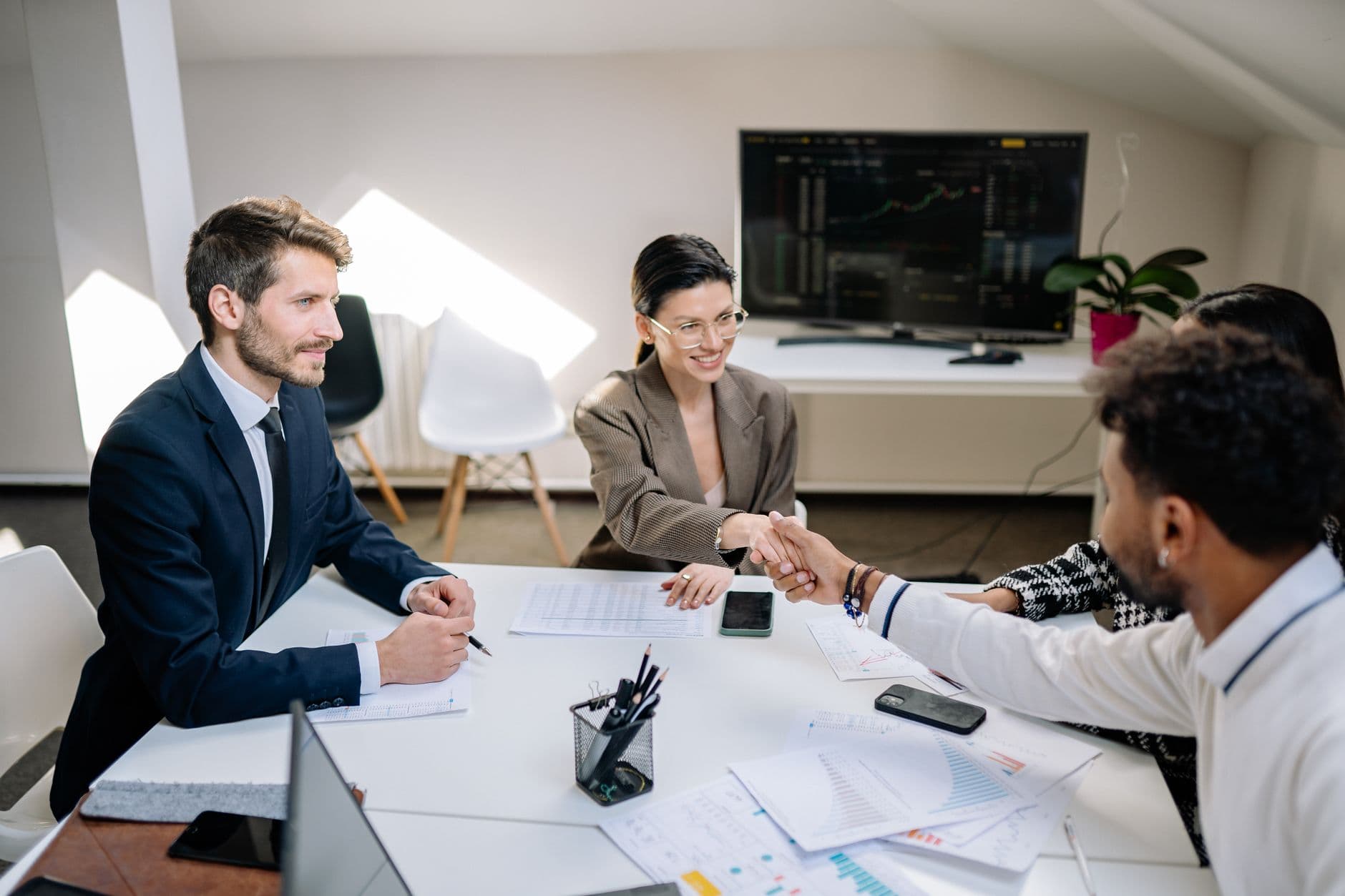 A diverse group of professionals in a business meeting shaking hands and discussing financial charts