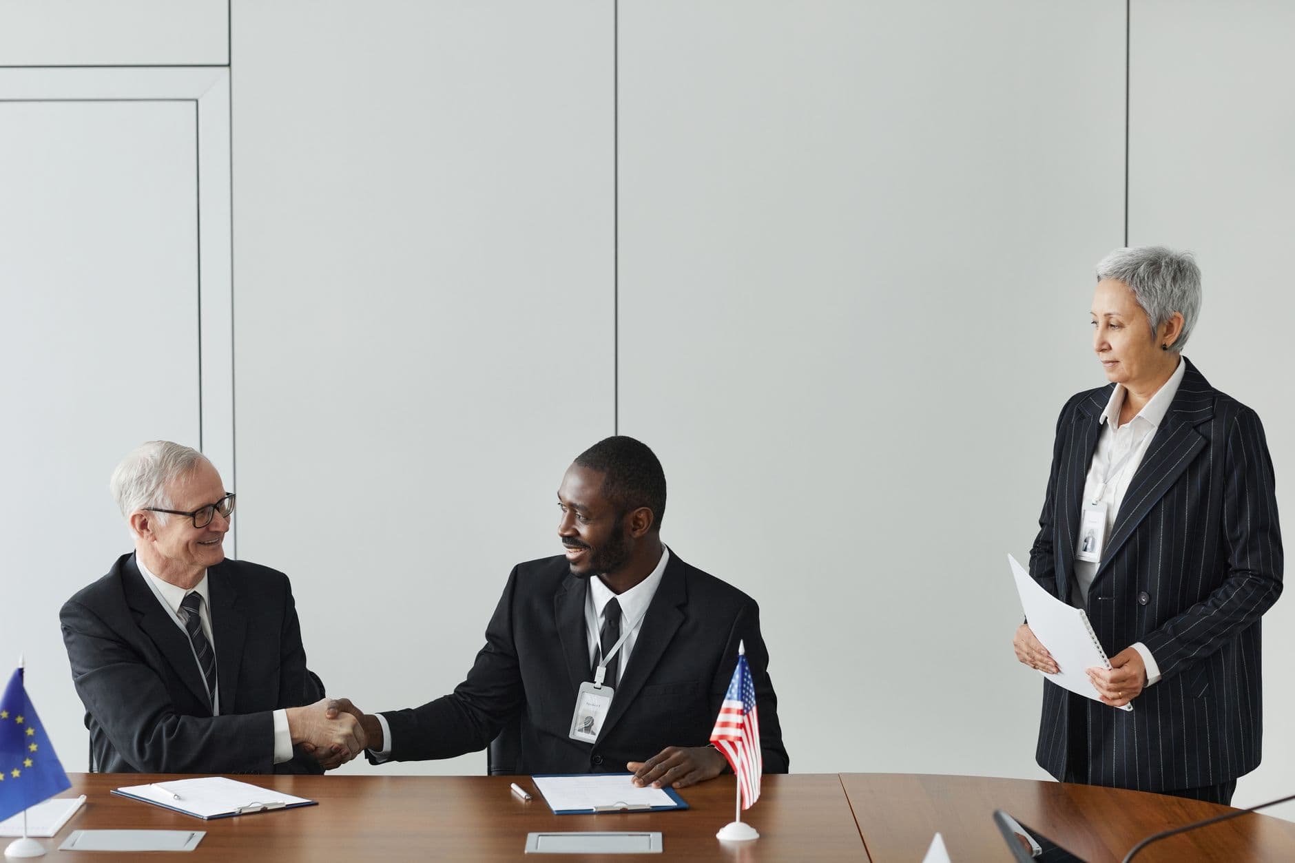 Business professionals shaking hands around a table with national flags in the background