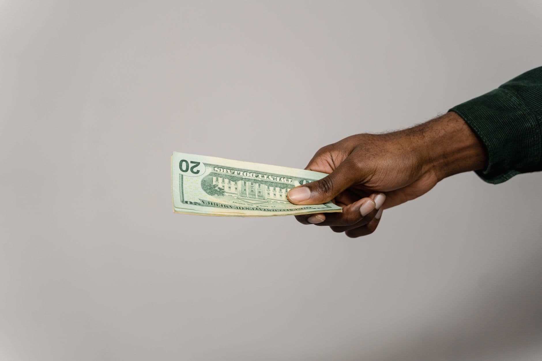 A hand holding a US dollar banknote against a plain background