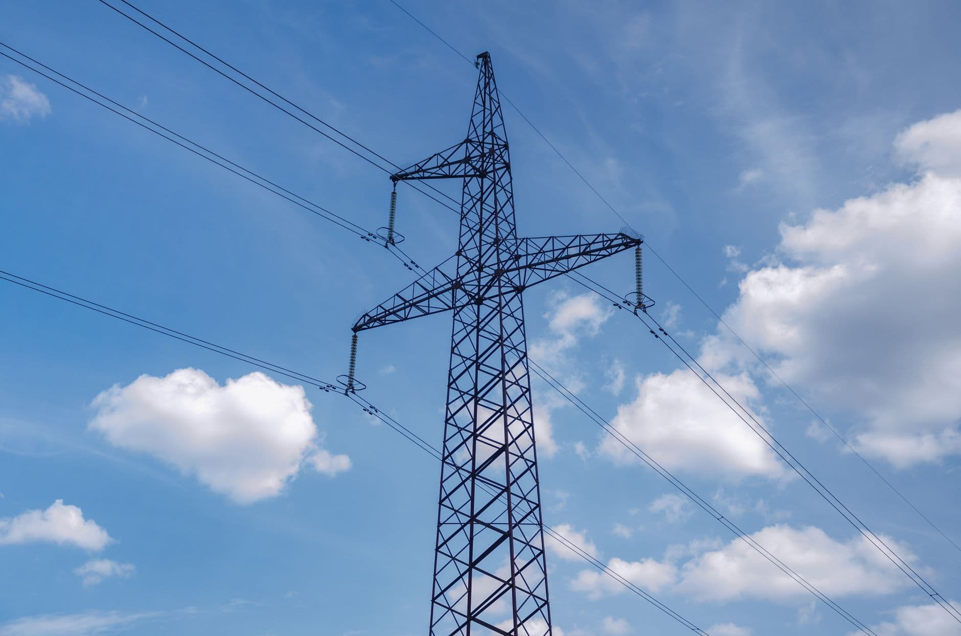 A high-voltage electricity transmission tower set against a bright blue sky