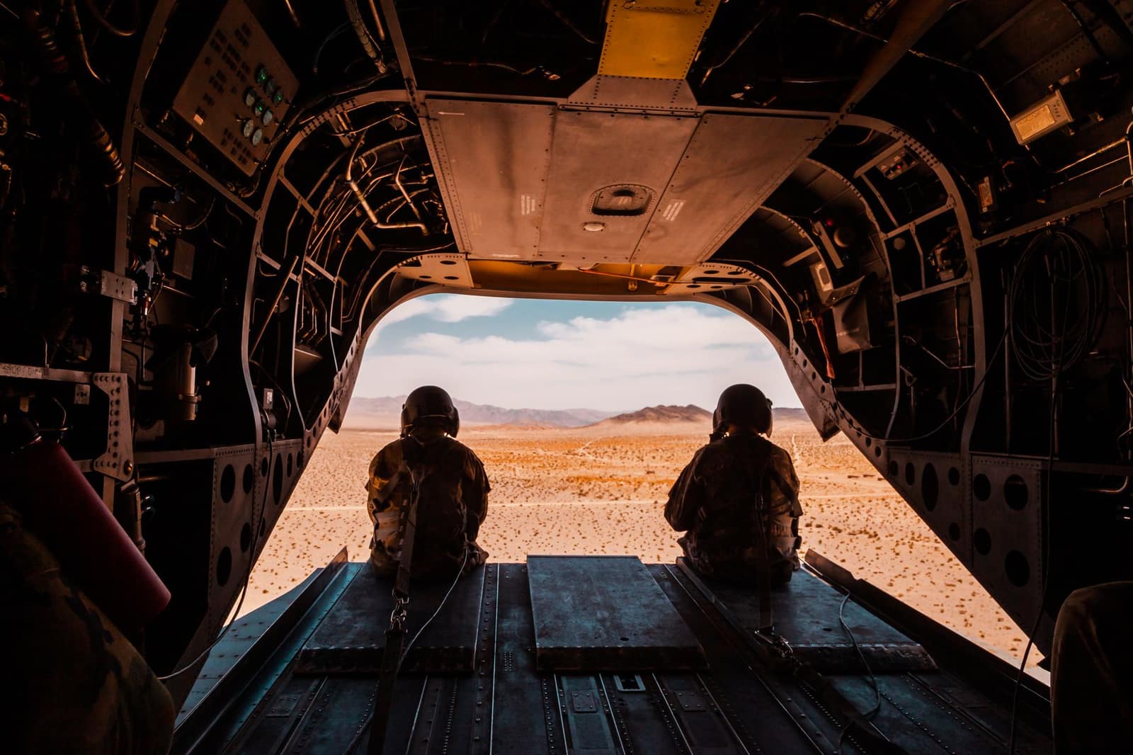 Soldiers seated in a military aircraft looking out over a desert landscape