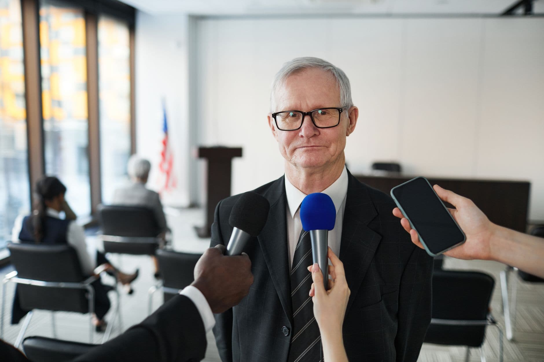 A man in formal attire being interviewed by media in a conference room