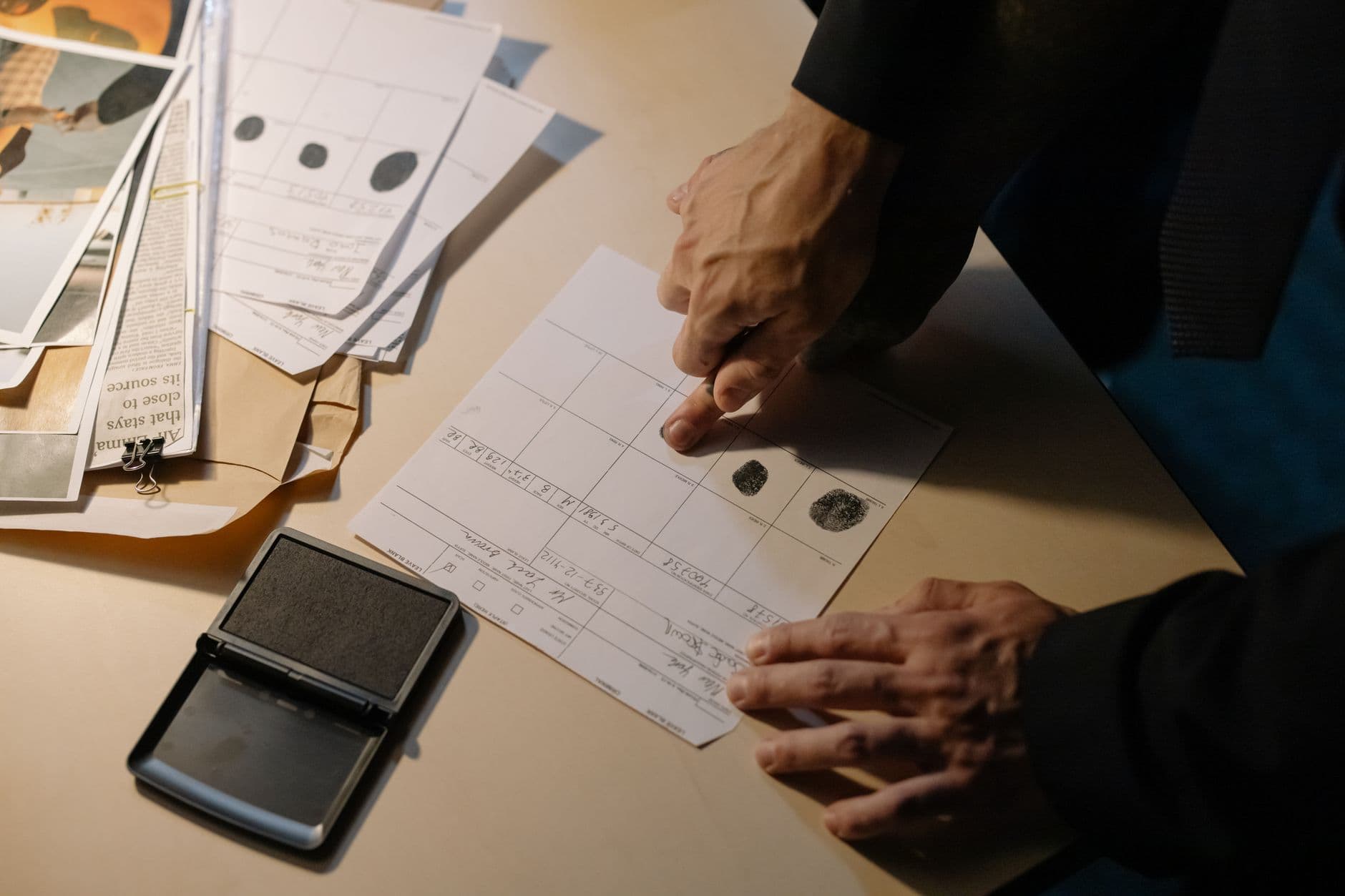 A person's hand pressing a fingerprint onto paper on a desk with an ink pad