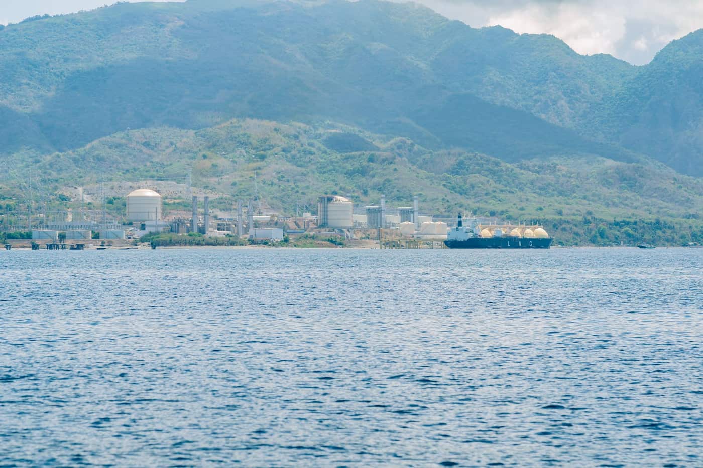 Industrial port facility with a docked LNG tanker against a mountain backdrop