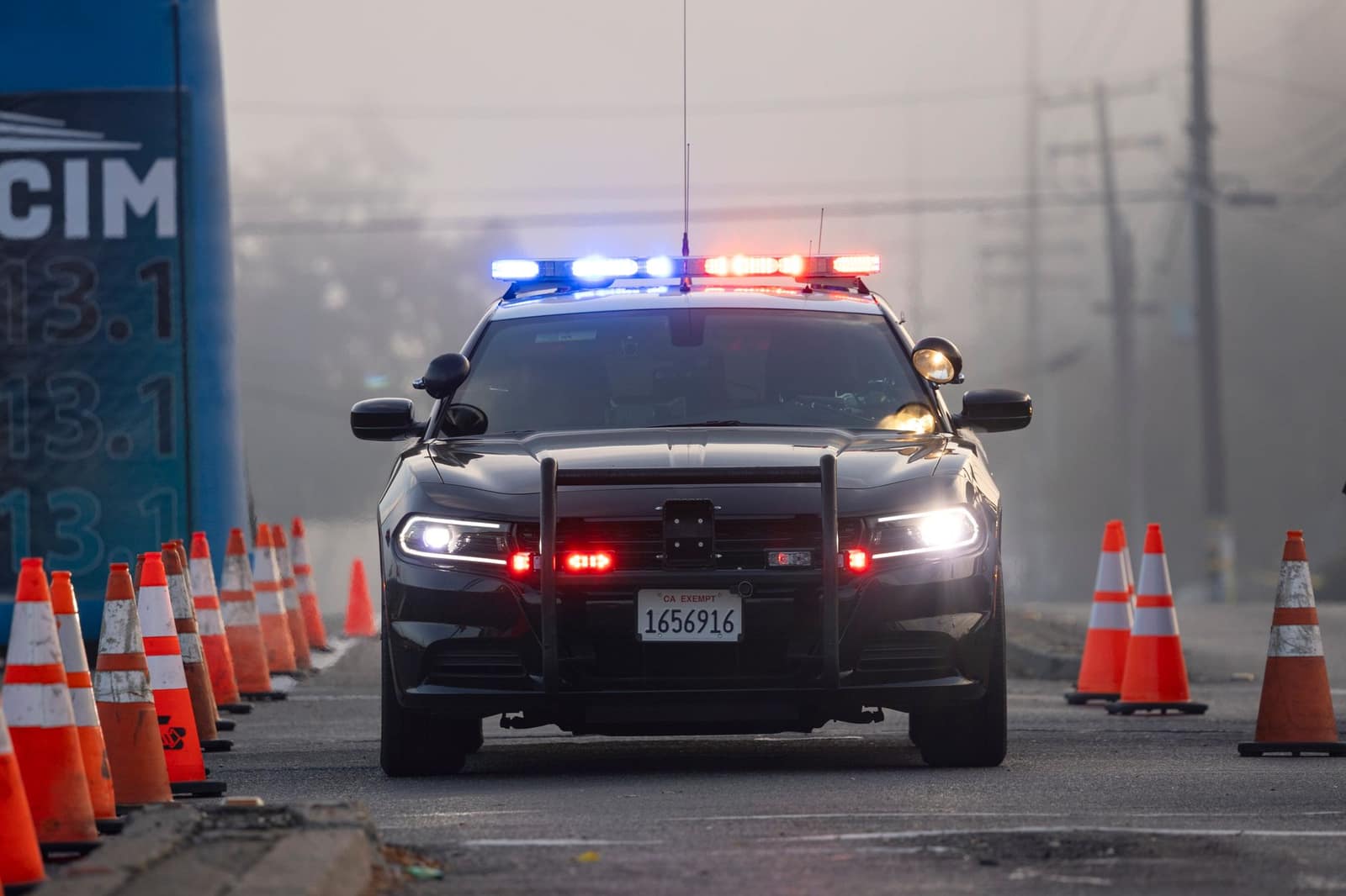 A police car with lights on parked at a roadside checkpoint surrounded by traffic cones