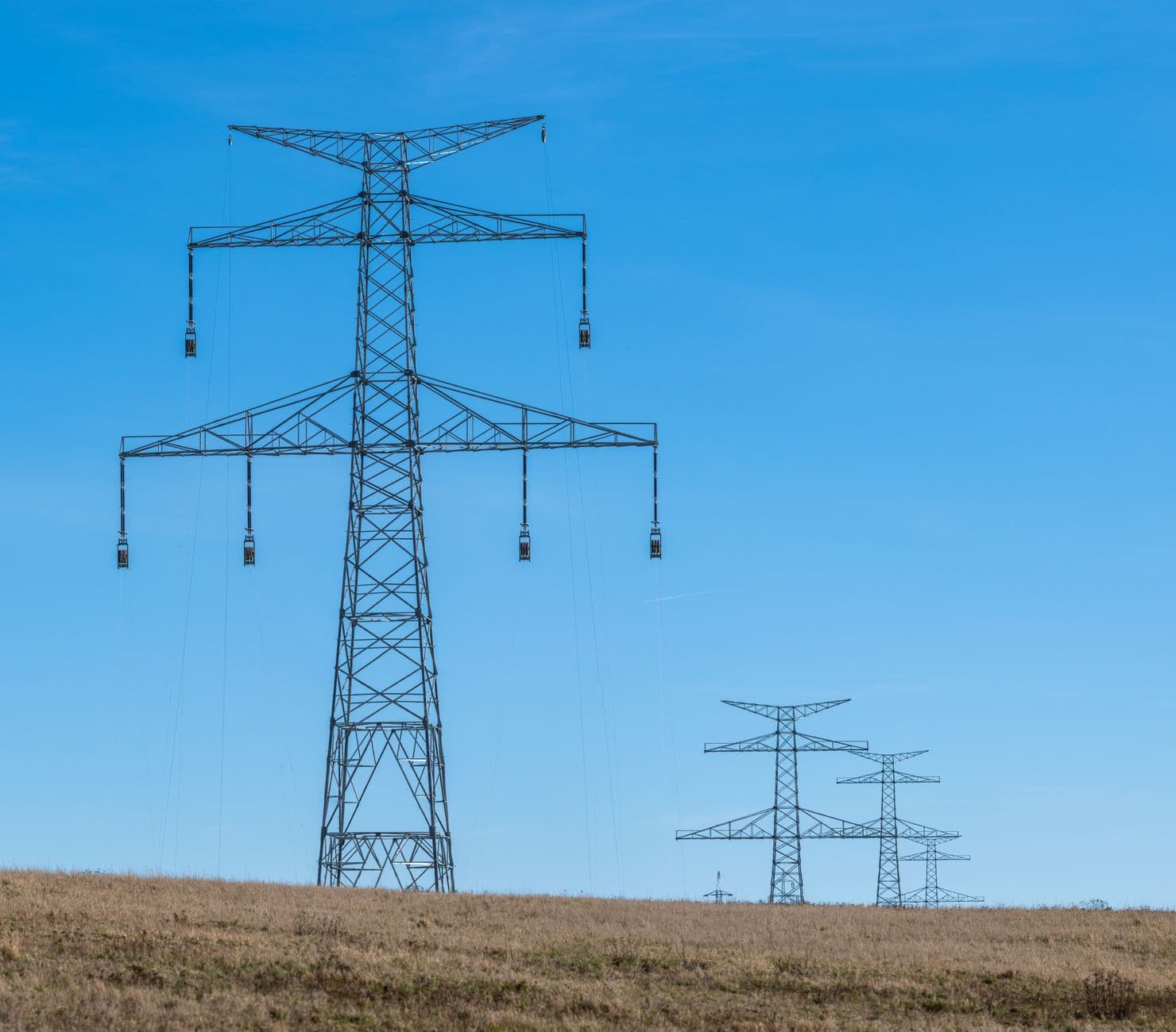 Electricity transmission pylons stretching across open countryside under a blue sky