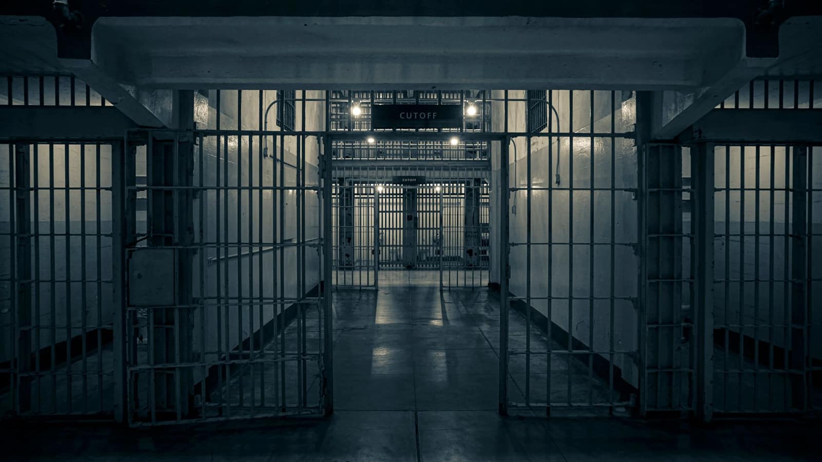 Moody interior of an empty prison corridor lined with metal bars